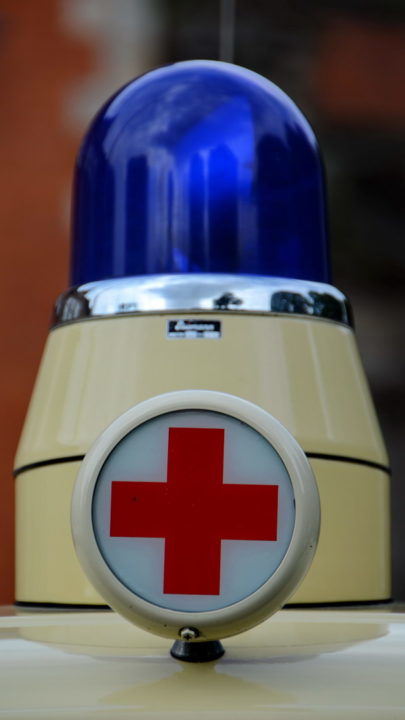 Ein altes Blaulicht auf einem Krankenwagen mit Rote-Kreuz-Zeichen davor